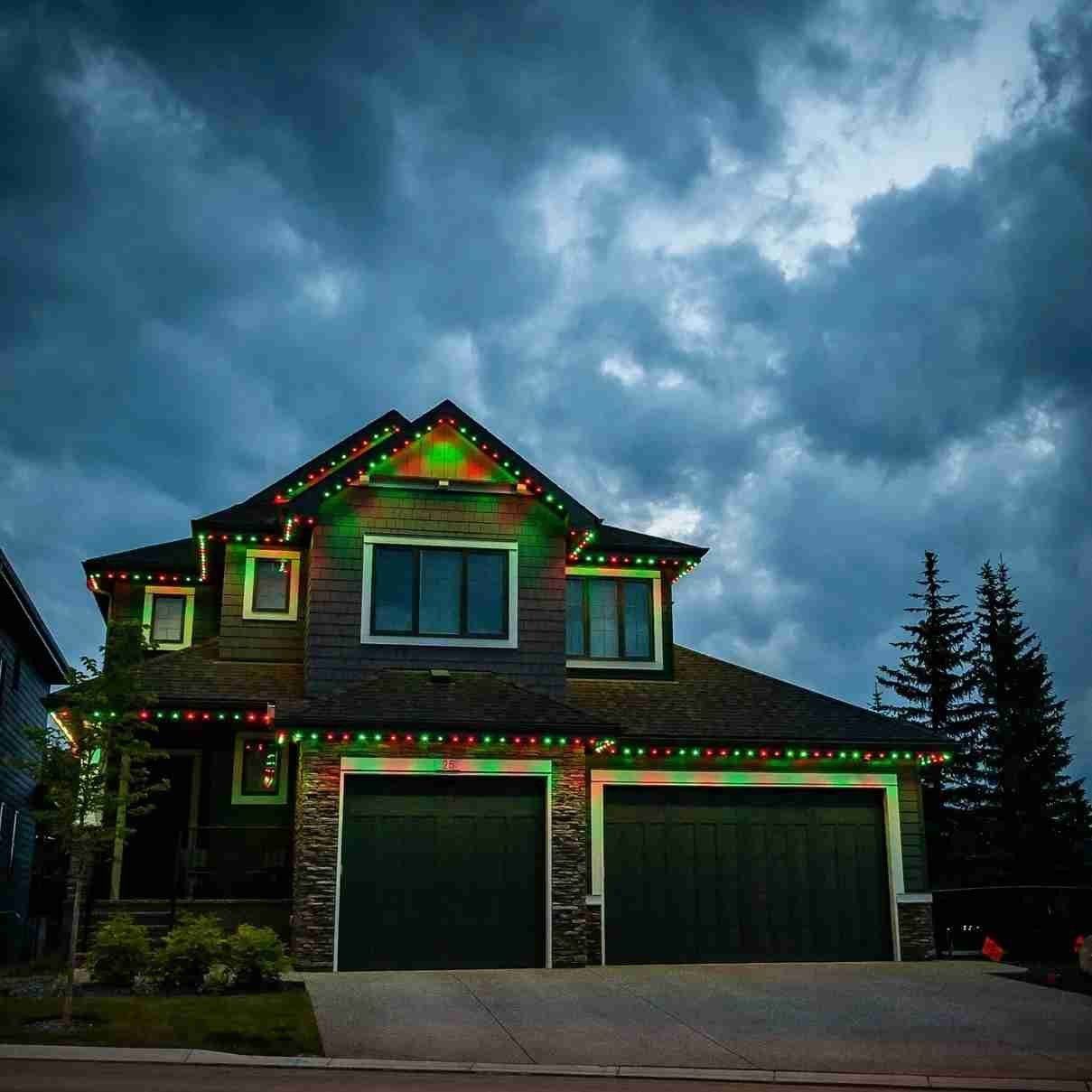 Red and green permanent Christmas lights on a two-story home under a stormy sky
